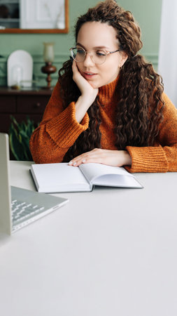 Contemplative Young Woman Taking Breaks from Online Learning and Working on Laptop at Home. Young Woman Studying and Working from Home, Lost in Thought and Contemplating Ideas on Her Laptop.の写真素材