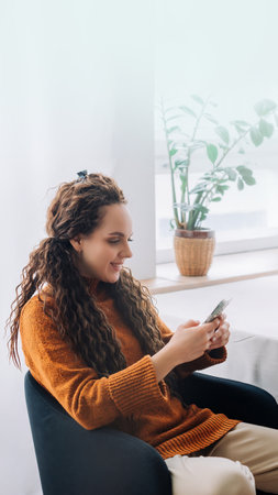 Modern Remote Worker: Happy Young Woman Using Smartphone and Laptop for E-learning and Remote Work at Home. Multi-tasking Young Woman Working from Home on Laptop and Cellphoneの写真素材