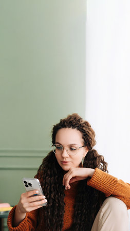 Stylish woman browsing on smartphone at home for online shopping. Young woman wearing glasses checking apps on cellphone at home. Happy woman using smartphone for online shopping and browsingの写真素材