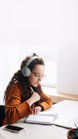 Young woman elearning from home, attending virtual class and remote conference meetings on laptop. Female student distance learning at home with laptop, headphones, and webinarsの写真素材