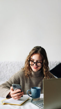 SMM specialist working from home at kitchen table, using smartphone to select blogger for product promotion in social media, in front of laptop. Influencer marketing conceptの写真素材