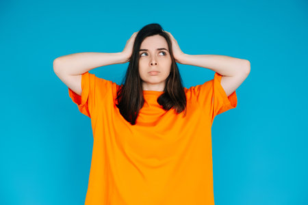 Stressed Young Woman Expressing Discontent, Touching Head - Negative Emotions, Frustration, Isolated Blue Backgroundの写真素材