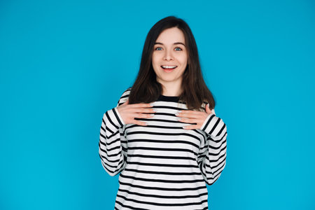 Portrait of a gorgeous, pretty, imposing girl in a striped pullover with her arms across her chest, isolated on a blue backgroundの写真素材
