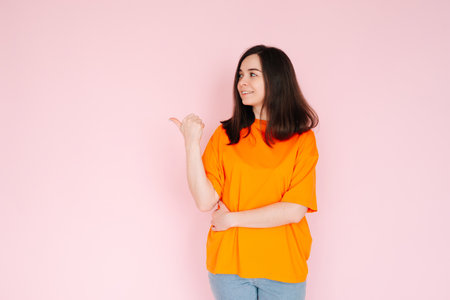 Alluring Advertising Space: Charming Lady Pointing Thumbs at Empty Area - Attention-Grabbing Concept for Promotional Opportunities on Pink Background.の写真素材