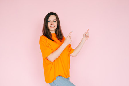 Inviting Emptiness: Cheerful Woman Pointing with Two Fingers to an Empty Space - Drawing Attention to Available Opportunities, Isolated on Pink Backgroundの写真素材