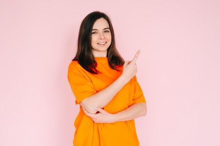 Playful Gestures: Charming Woman Pointing Finger at Empty Space - Humor and Interaction Concept, Isolated on Pink Background.の写真素材