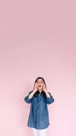 Portrait of young woman with joyous expression, hands near open mouth as if sharing news or telling a funny story, beaming a big toothy smile, isolated on bright pink background. Vertical photographyの写真素材