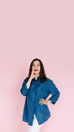 Excited Girl Sharing Breaking News: Hand Near Open Mouth Conveying Surprise and Delivering Important Information in an Empty Space, Isolated on a Pink Background.の写真素材