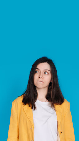 Serene Young Woman Contemplating, Gazing into Empty Space, Thoughtful Young Woman in Captivating Portrait, Lost in Contemplation, Isolated on Blue Backgroundの写真素材