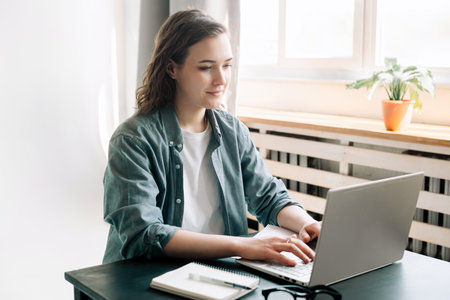 Young woman multitasking with a laptop in a modern office environment and student girl focused on work from home. Online work, study, freelance, business, and office lifestyle conceptの写真素材