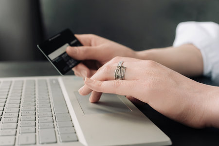 Graceful Online Shopping: Woman's Hands Holding Credit Card, Engaging in E-commerce with Laptop - Conceptual Image. Convenience of Online Shopping: Woman's Hands, Credit Card, and Laptop.の写真素材