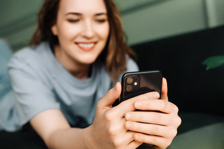 A cheerful young middle-aged woman is typing on her smartphone, watching a video, reading a message. Multitasking Maven. Middle-aged Woman Engaged in Smartphone Activities.の写真素材