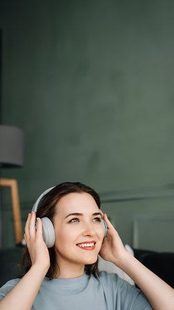 A smiling young middle-aged woman wearing wireless headphones listens to music. Musical Bliss. Middle-Aged Woman Embracing Joy Through Wireless Headphones. Rhythmic Escape.の写真素材