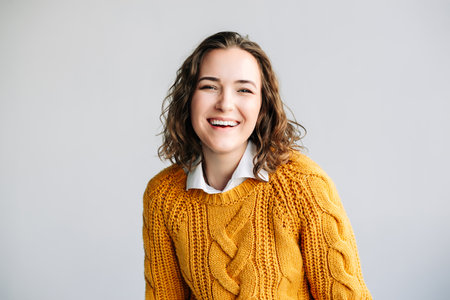 Charming young woman with curly hair, smiling and looking at the camera. She exudes positivity and...