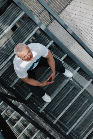 A man is standing on a staircase with his hands on his hips. He is wearing a white shirt and black pants.の写真素材