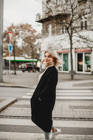 A woman wearing a black coat and scarf is standing on a crosswalk. She is smiling and looking to her rightの写真素材