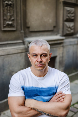 A man with a white shirt and blue stripes stands in front of a wall. He is looking at the camera with a serious expressionの写真素材