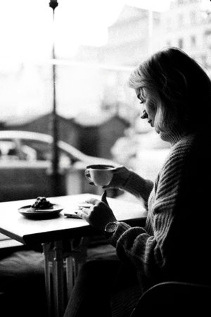 A woman sits at a table with a cup of coffee in front of her. She is wearing a sweater and she is enjoying her coffeeの写真素材