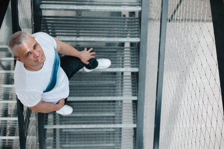 A man is standing on a set of stairs with a smile on his face. He is wearing a white shirt and blue jeansの写真素材