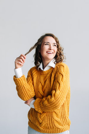Joyful Young Woman. Smiling, Beautiful, and Positive. Cheerful, Pretty, and Cute Curly-haired Student. Laughing, Playing with Hair. Portrait of Happiness and Confidence - Isolated on White Background.の写真素材