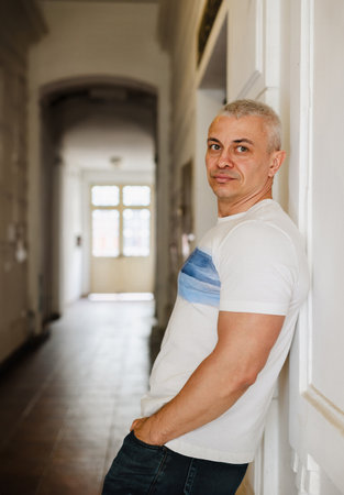 A man stands in a hallway wearing a white shirt with a blue stripe. He is looking at the camera with a serious expressionの写真素材