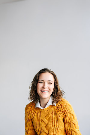 Charming young woman with curly hair, smiling and looking at the camera. She exudes positivity and joy, standing isolated against a white background in a close-up headshot portrait.の写真素材