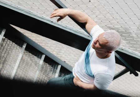 A man wearing a white shirt and gray pants is leaning on a railing. He is looking up at something, possibly a bird or a person. The image has a casual and relaxed moodの写真素材