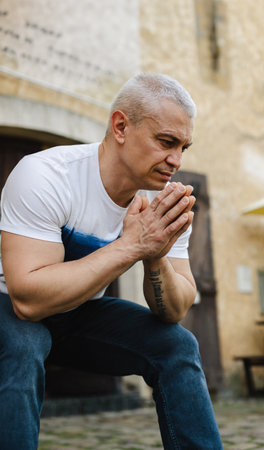 A man is praying in front of a building. He is wearing a white shirt and blue jeansの写真素材