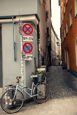 An old bicycle with a flower pot leans against a field with traffic signs in a picturesque European alley. The cobblestone street and historic buildings create a nostalgic urban atmosphereの写真素材