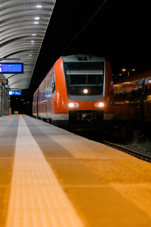 Red modern passenger train waiting at night station platform, representing travel, urban commuting, and transportation infrastructureの写真素材