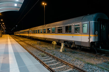 Passenger train standing at a night railway station platform, representing travel, transportation,...