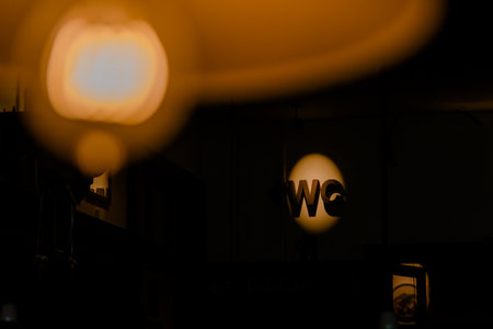 A dimly lit "WC" sign stands out in a dark, atmospheric interior, with a soft, out-of-focus light in the foreground. Captures a sense of mystery and modern design for public facilities.の写真素材