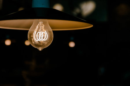 Warm glowing light bulb with visible filament suspended in dark interior, creating a cozy minimal...