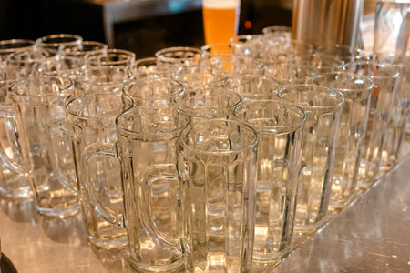 Many sparkling clean, empty beer mugs waiting on a polished counter. Ideal for showcasing a bar, brewery, or pub environment, hinting at social gatherings and refreshment.の写真素材