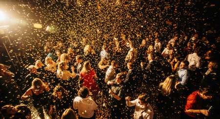 High angle view of a large crowd dancing under a shower of golden confetti. This energetic scene captures the climax of a party, perfect for promoting a wedding, concert, or New Year's Eve event.の素材