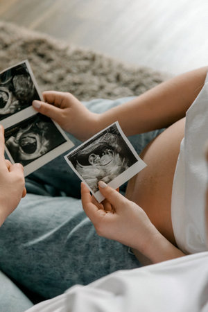 A pregnant woman holds several ultrasound photos near her belly. This image represents the joy and...