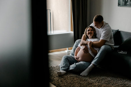 Pregnant woman and man sitting on floor embracing. They share a tender and joyful moment during pregnancy. Perfect for family planning, parenthood, or lifestyle content.の写真素材