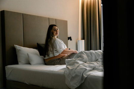A happy pregnant woman sits on a cozy bed in a modern bedroom. The mood is calm and peaceful....
