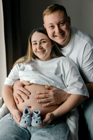 A happy pregnant woman and her husband holding baby boots. They are smiling and showing anticipation...