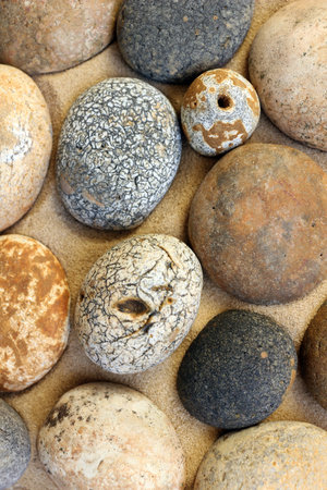 Collection of round pebbles with different colours and textures on sandy surface, closeup