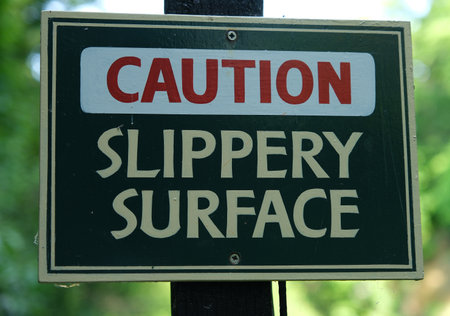 Close-up of a Caution Slippery Surface sign warning pedestrians of potential hazard in outdoor area.の写真素材