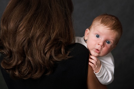 The kid sits on his mother's arms and looks out over her shoulder.の写真素材