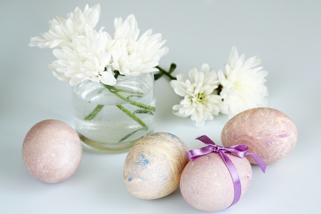 On a light background painted Easter eggs. Near a a bouquet of chrysanthemumsの写真素材