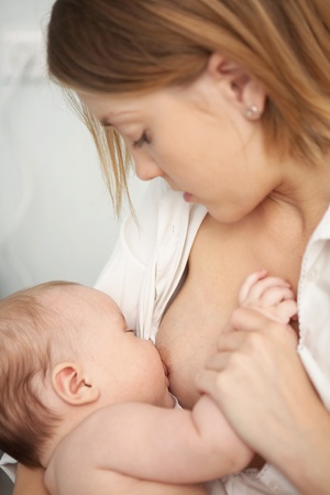 A woman looks at the baby sucking the breast and holding his handの写真素材