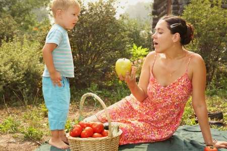 young woman with her little son are on the grass in the garden  Near basket with tomatoes and cucumbers の写真素材