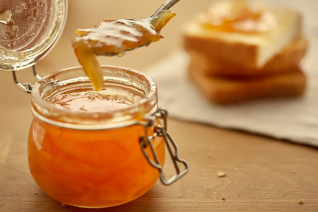 Glass jar with orange jam.In the background are toast of white bread.