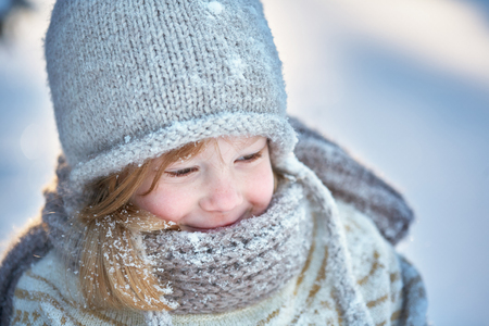 Little girl in a sweater sits in the snow and smiles.の写真素材
