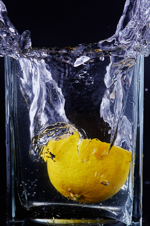 Half a lemon is in a glass vessel with water. Drops, trickles, air bubbles.の写真素材