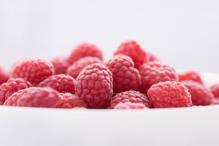 Red berries are in a white bowl on white backgroundの写真素材