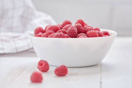 Red berries are in white bowl on white tableの写真素材